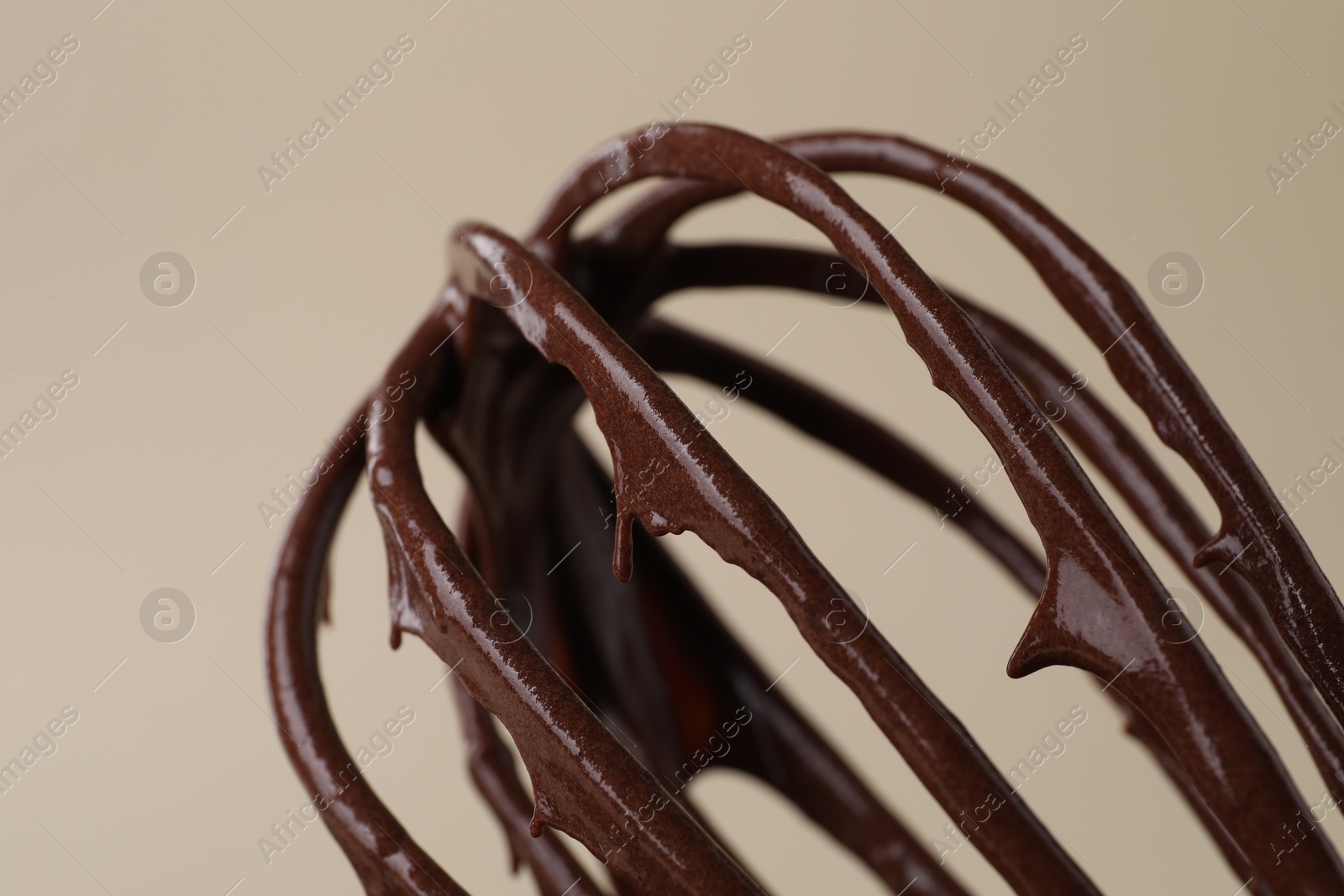 Photo of Whisk with chocolate cream on beige background, closeup