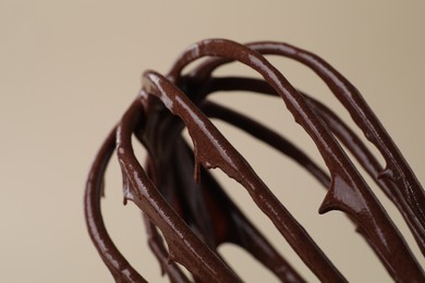 Whisk with chocolate cream on beige background, closeup