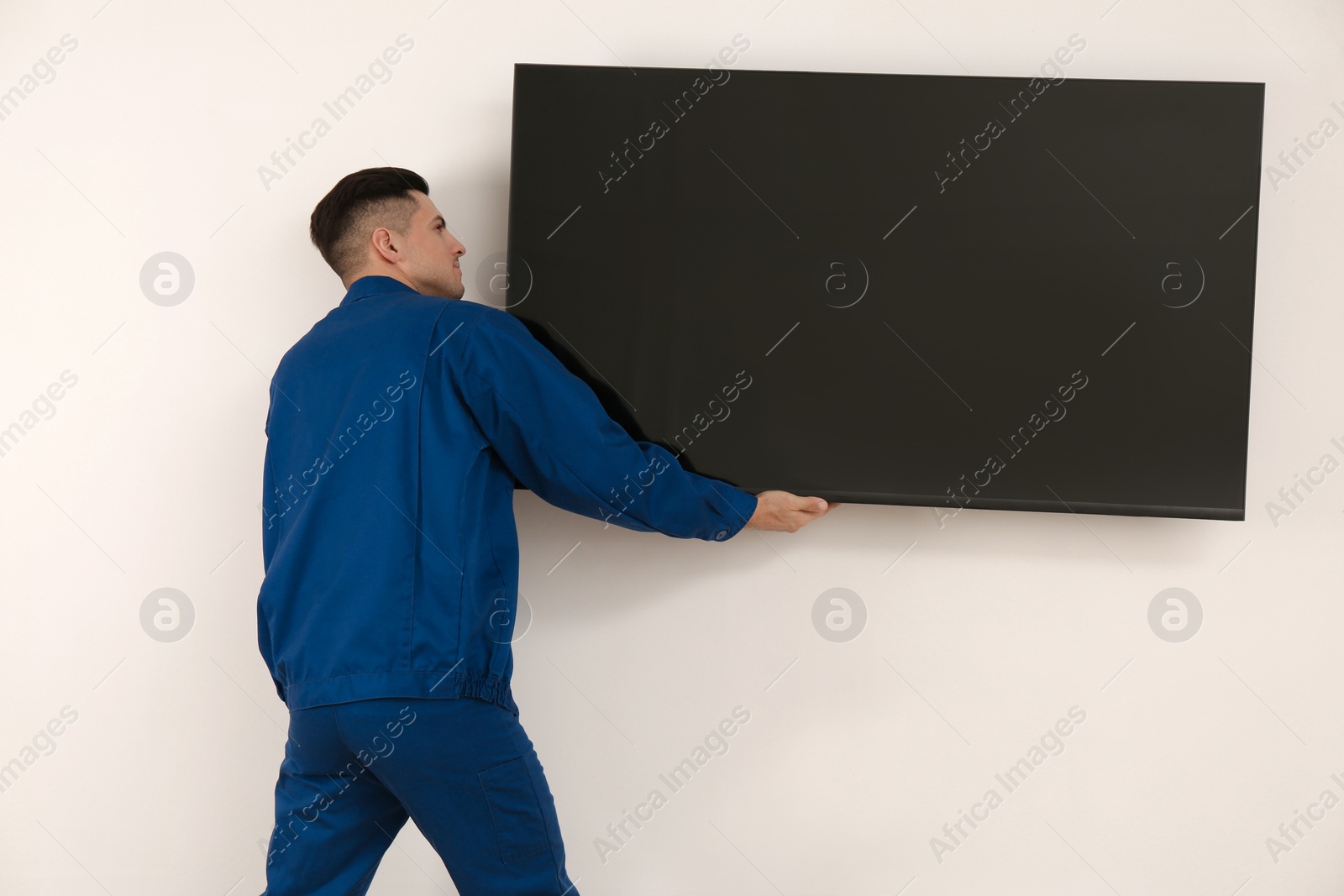 Photo of Professional technician installing modern flat screen TV on wall indoors