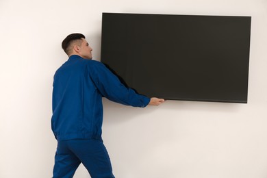 Photo of Professional technician installing modern flat screen TV on wall indoors