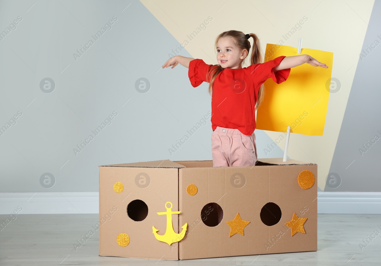 Photo of Cute little child playing with cardboard ship near color wall