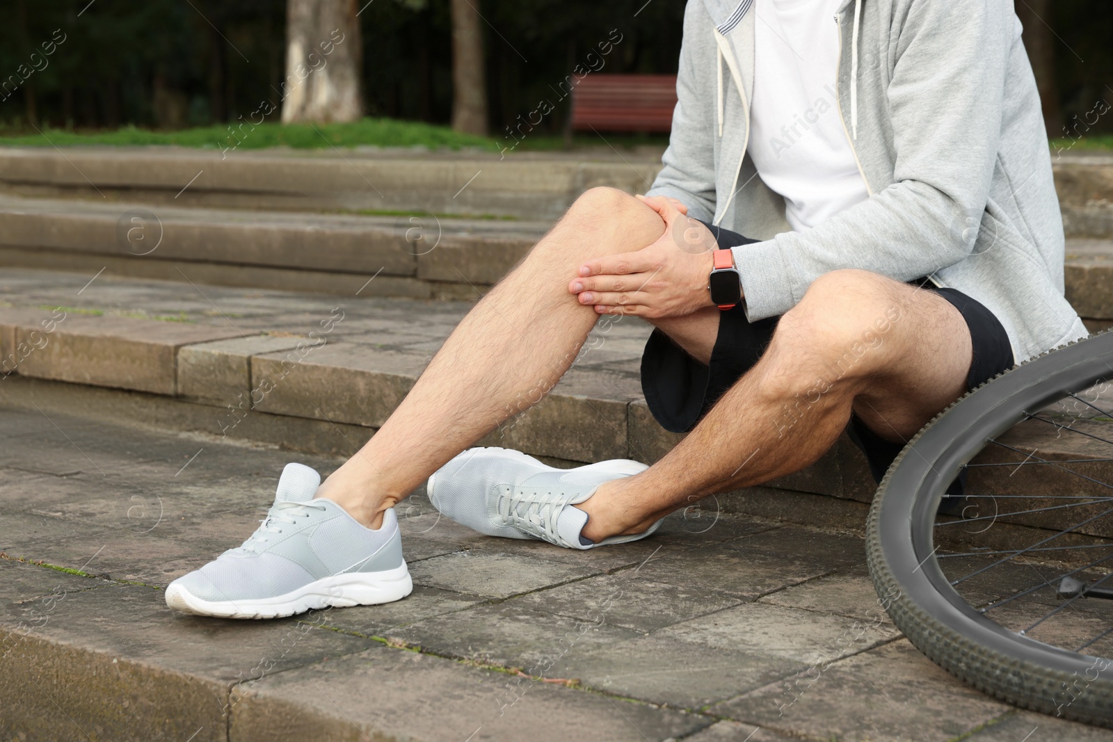 Photo of Man with injured knee on steps near bicycle outdoors, closeup