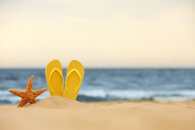 Photo of Yellow flip flops and starfish in sand near sea, space for text. Beach objects