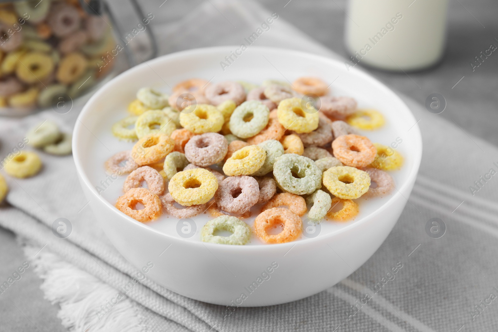 Photo of Tasty colorful cereal rings and milk in bowl on table, closeup