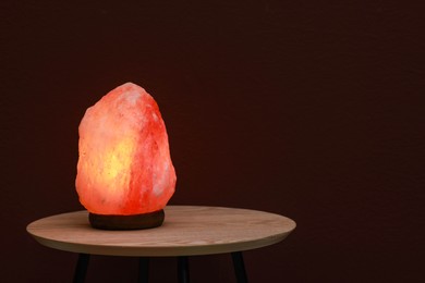 Photo of Himalayan salt lamp on wooden table near brown wall, space for text