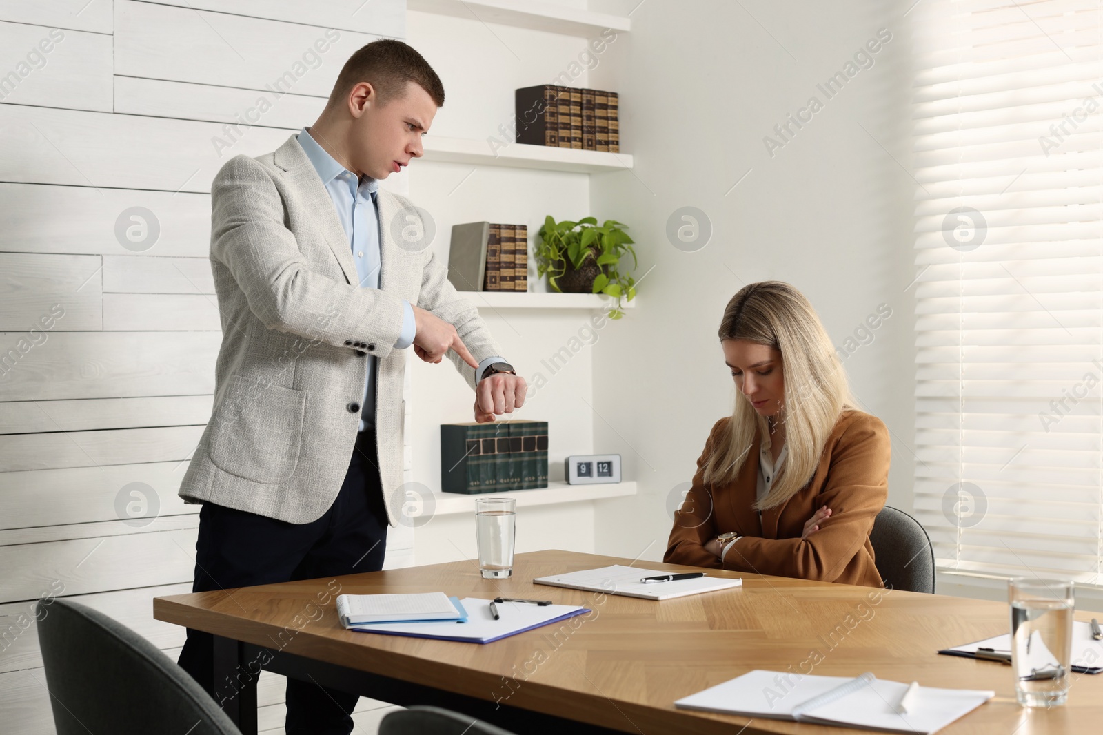 Photo of Businessman pointing on wrist watch while scolding employee for being late in office