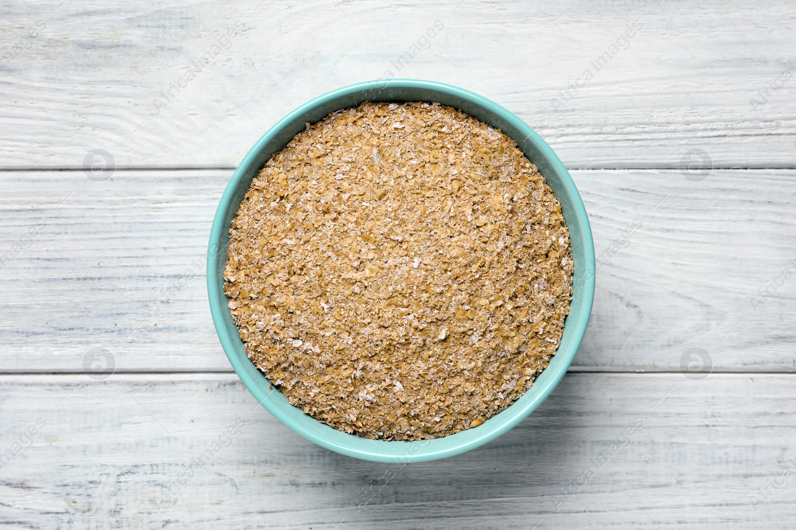 Photo of Bowl of wheat bran on white wooden table, top view