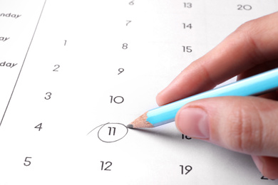 Photo of Woman marking date in calendar with pencil, closeup