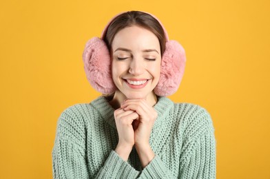 Photo of Happy woman wearing warm earmuffs on yellow background