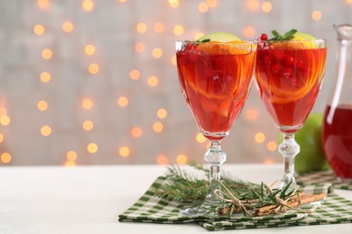 Photo of Christmas Sangria cocktail in glasses, cinnamon sticks and fir tree branch on white table against blurred lights. Space for text