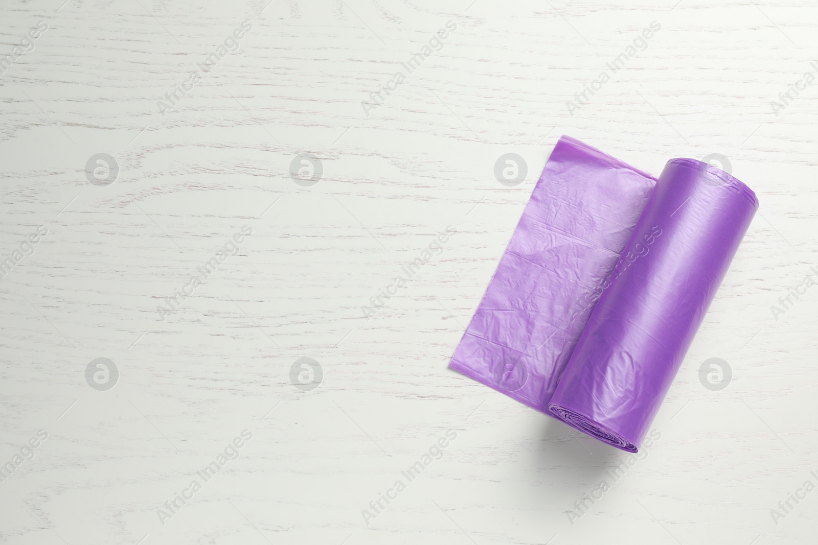 Photo of Roll of violet garbage bags on white wooden table, top view. Space for text
