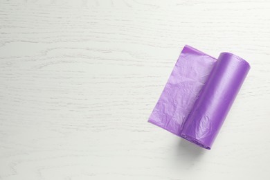 Roll of violet garbage bags on white wooden table, top view. Space for text