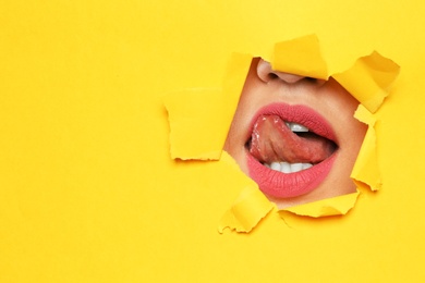 Photo of Lips of young woman with beautiful lipstick visible through hole in color paper. Space for text