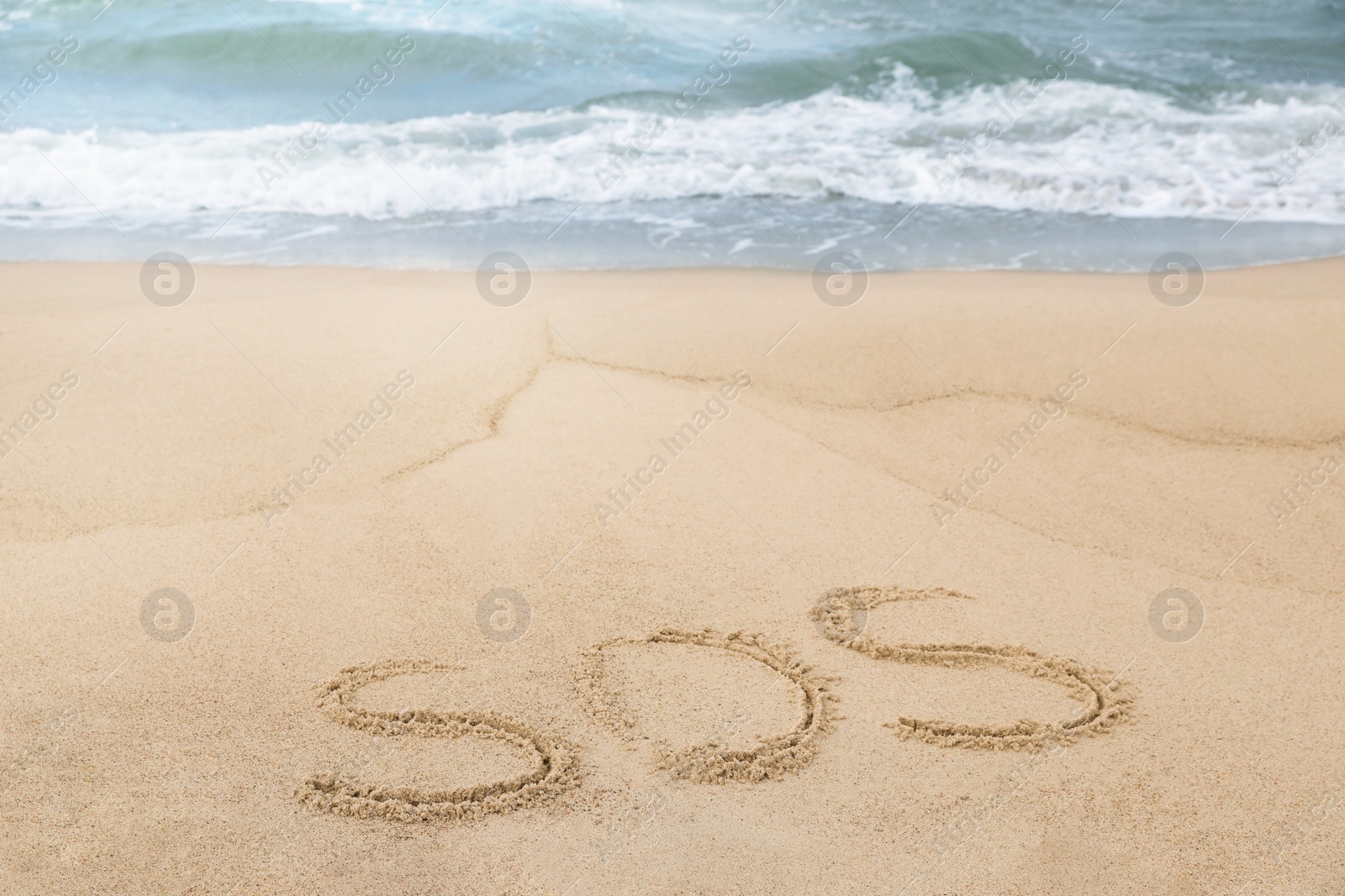 Photo of Message SOS drawn on sand near sea