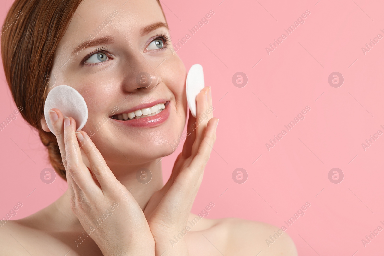 Photo of Smiling woman with freckles wiping face on pink background, closeup. Space for text