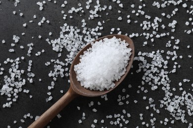 Photo of Natural salt and wooden spoon on black table, top view