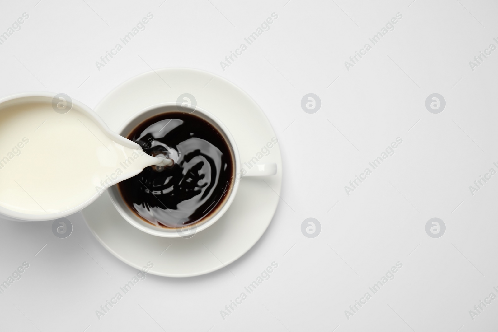 Photo of Pouring milk into cup of coffee on white background, top view