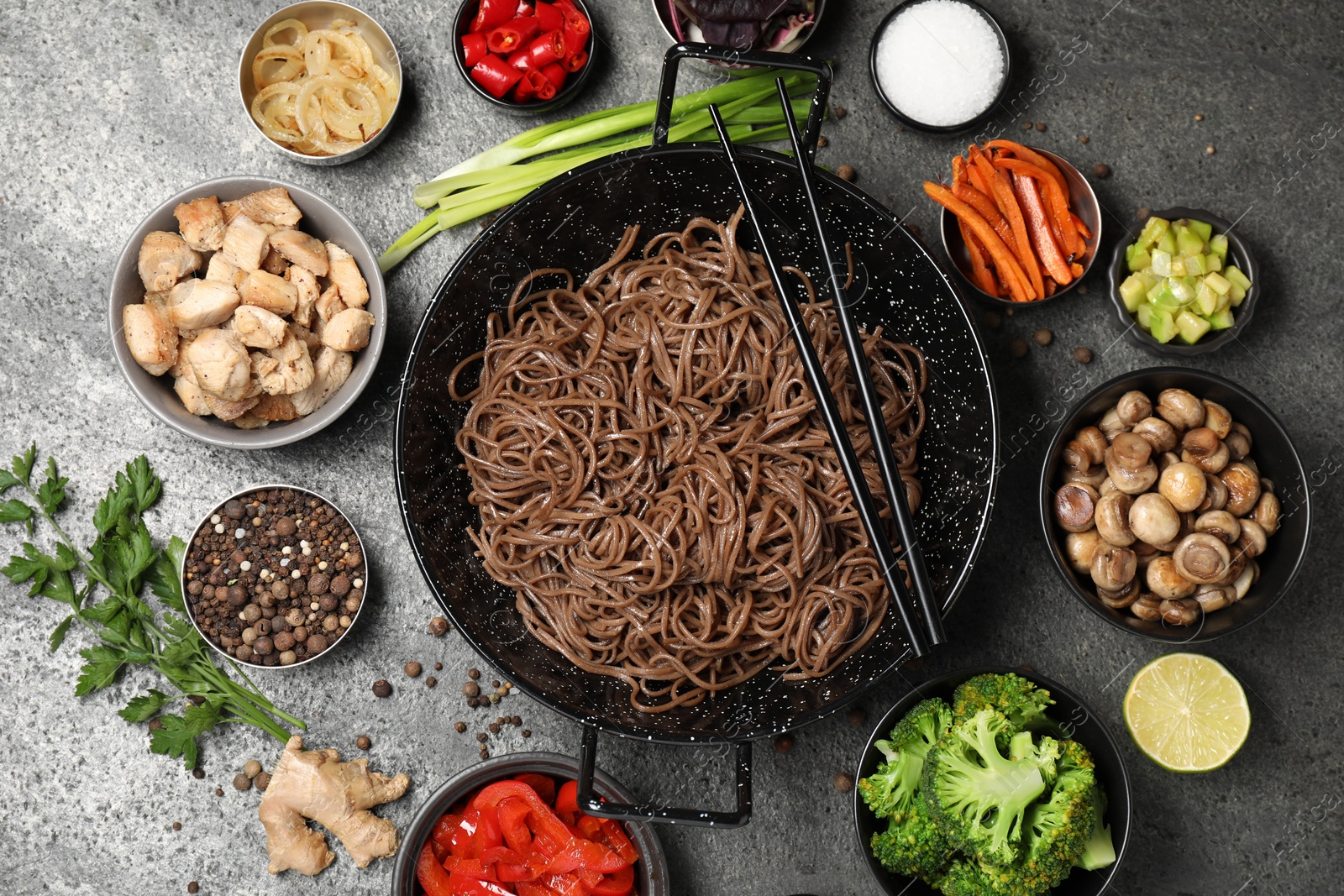 Photo of Wok with noodles, chicken and other products on grey table, flat lay