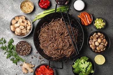 Wok with noodles, chicken and other products on grey table, flat lay