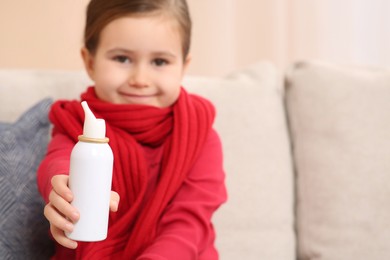 Photo of Cute little girl showing nasal spray indoors, focus on bottle. Space for text