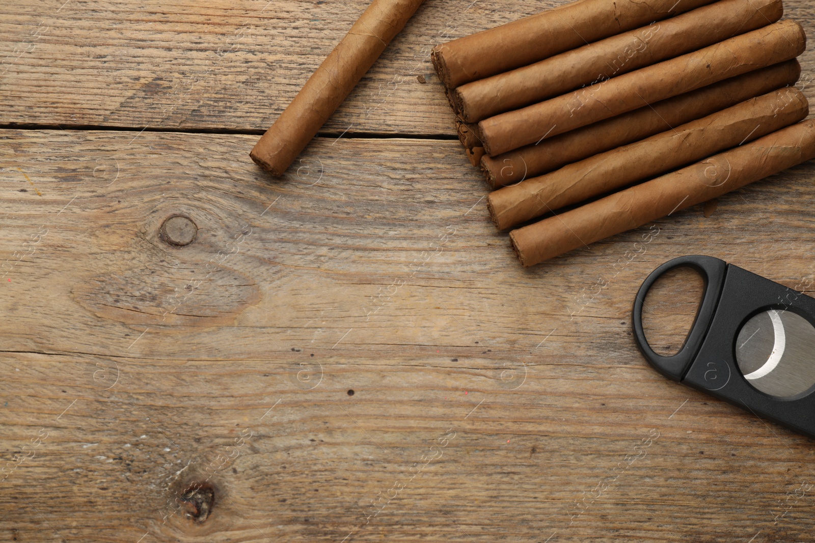 Photo of Cigars and guillotine cutter on wooden table, flat lay. Space for text