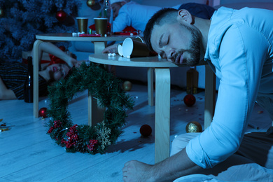 Photo of Drunk man sleeping at table in messy room after New Year party