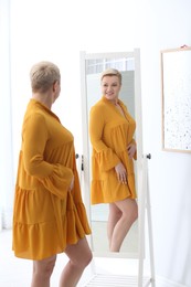 Photo of Beautiful mature woman looking at herself in large mirror indoors