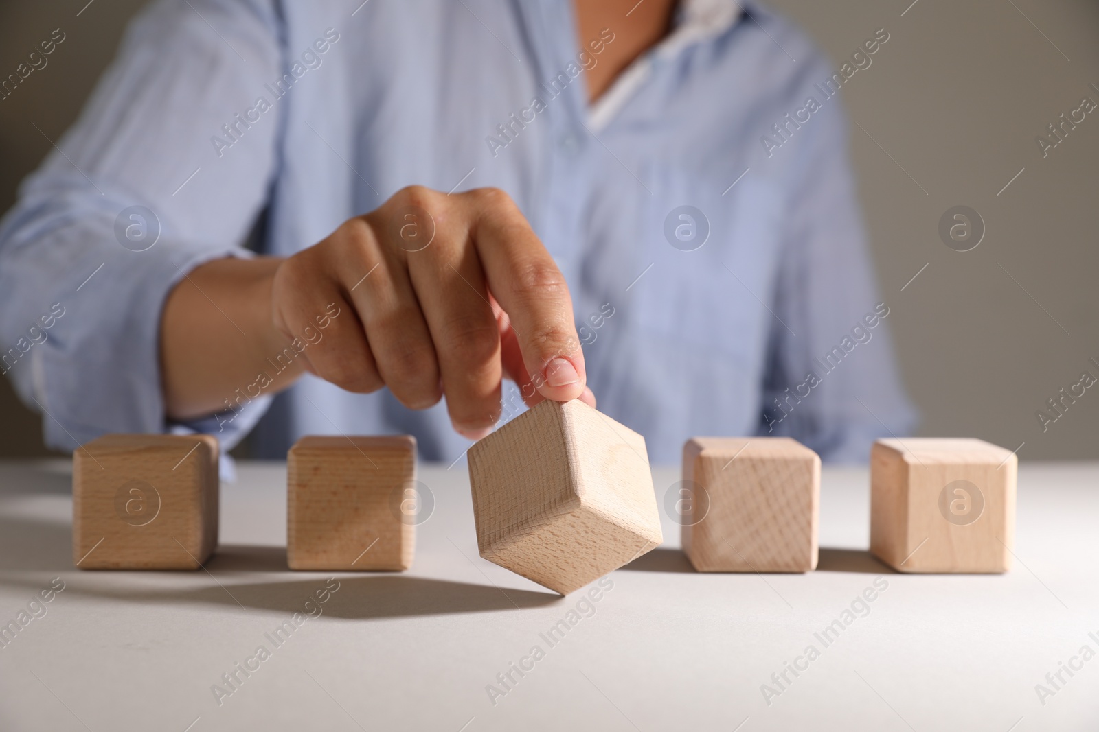 Photo of Woman choosing wooden cube among others at white table, closeup