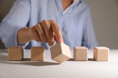 Woman choosing wooden cube among others at white table, closeup