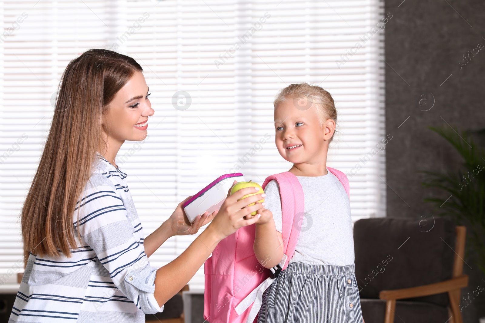 Photo of Young mother putting lunch into her little child's school bag at home