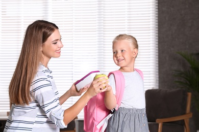 Young mother putting lunch into her little child's school bag at home