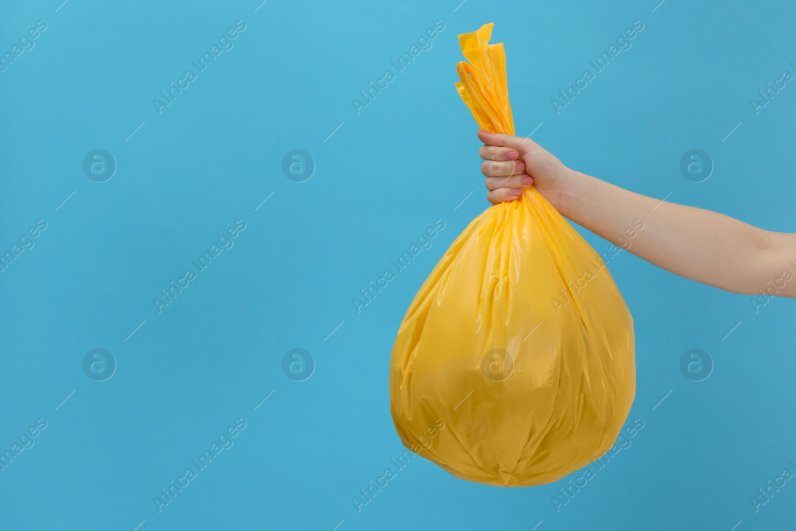 Photo of Woman holding plastic bag full of garbage on light blue background, closeup. Space for text