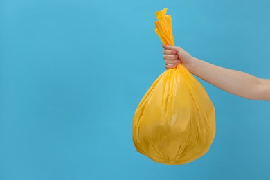 Photo of Woman holding plastic bag full of garbage on light blue background, closeup. Space for text