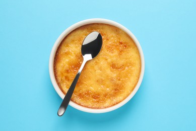 Photo of Delicious creme brulee and spoon in ceramic ramekin on light blue background, top view
