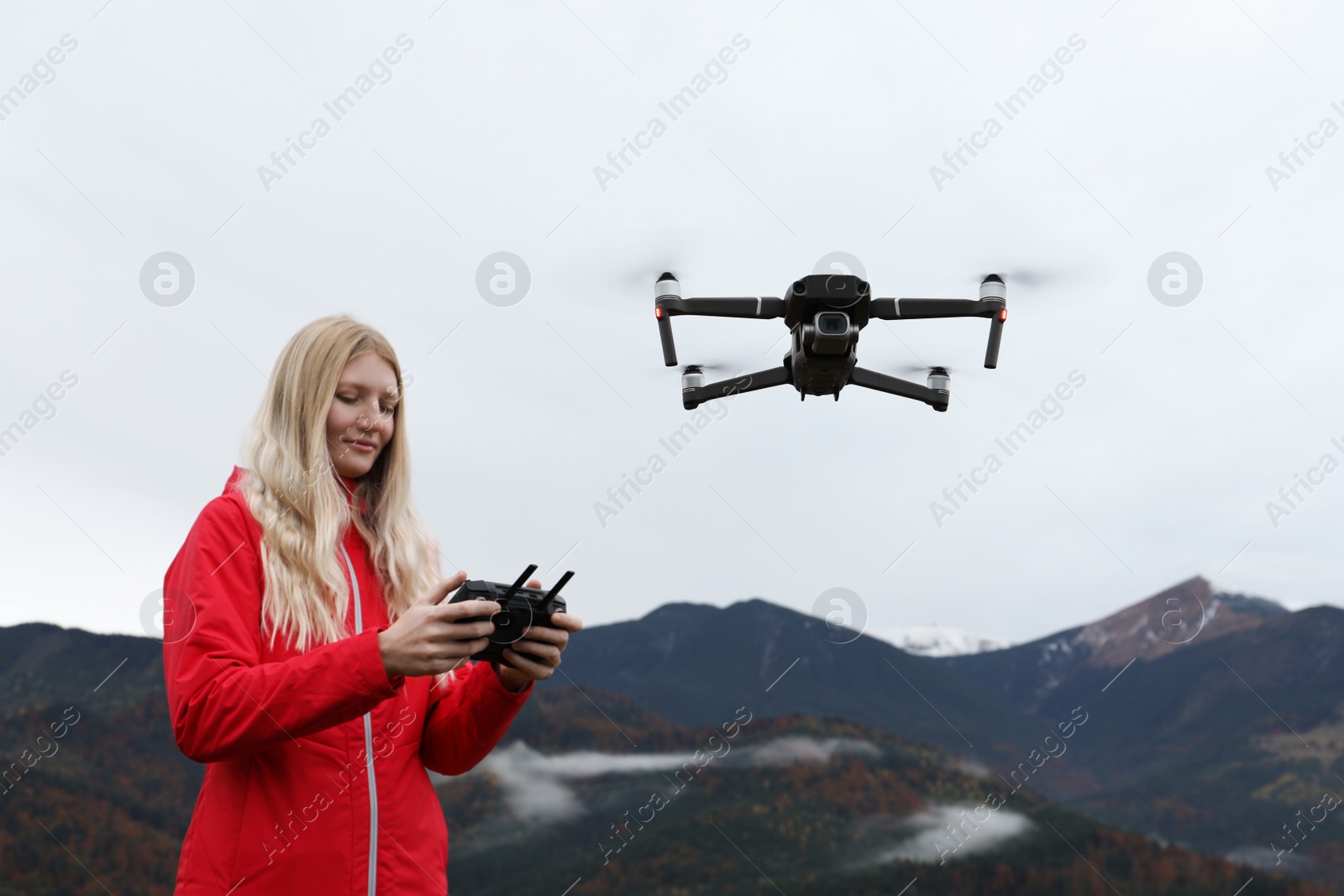 Photo of Young woman operating modern drone with remote control in mountains