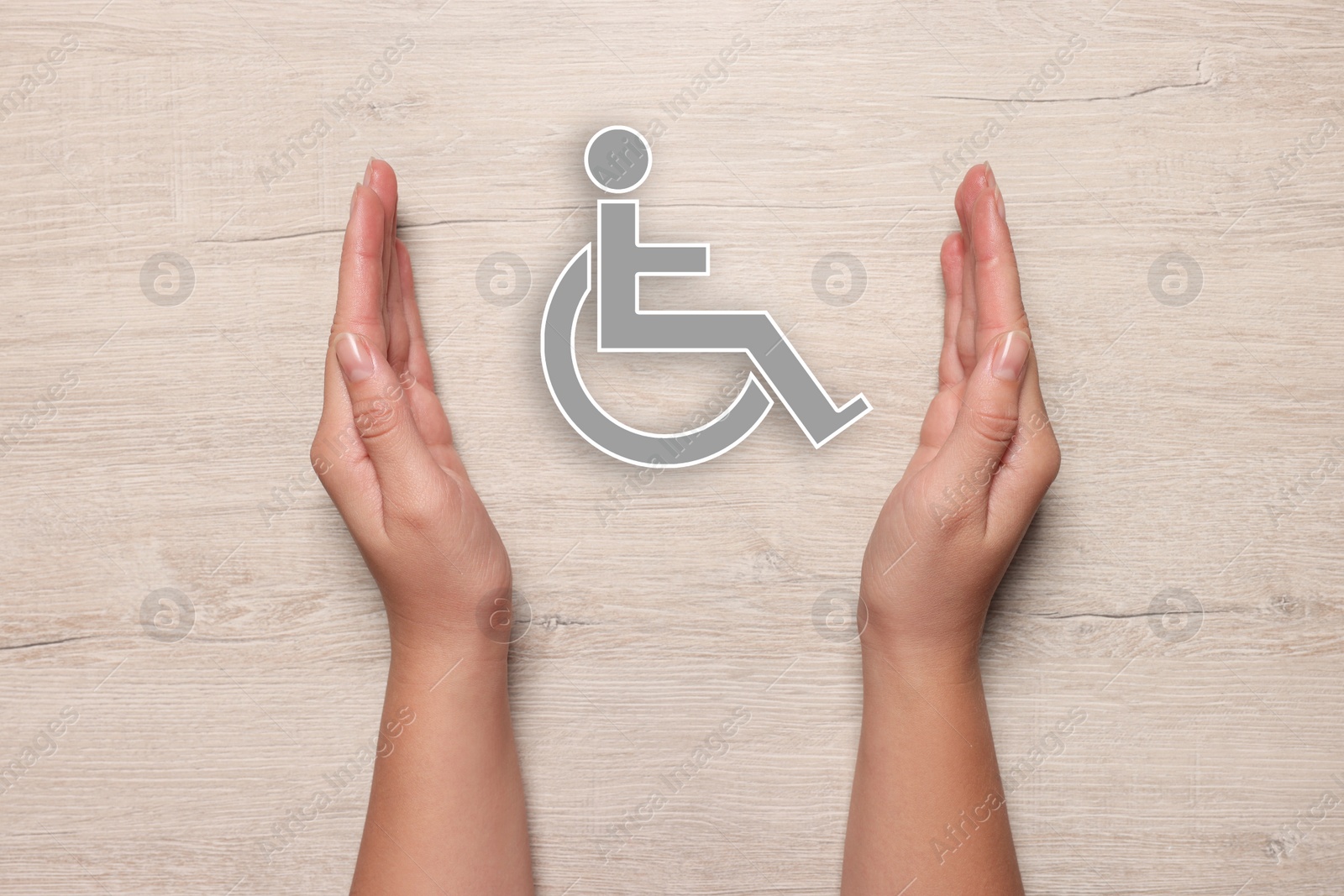 Image of Disability inclusion. Woman protecting wheelchair symbol on white wooden background, closeup