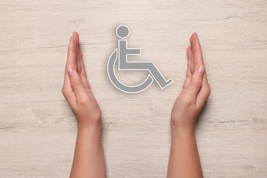 Image of Disability inclusion. Woman protecting wheelchair symbol on white wooden background, closeup