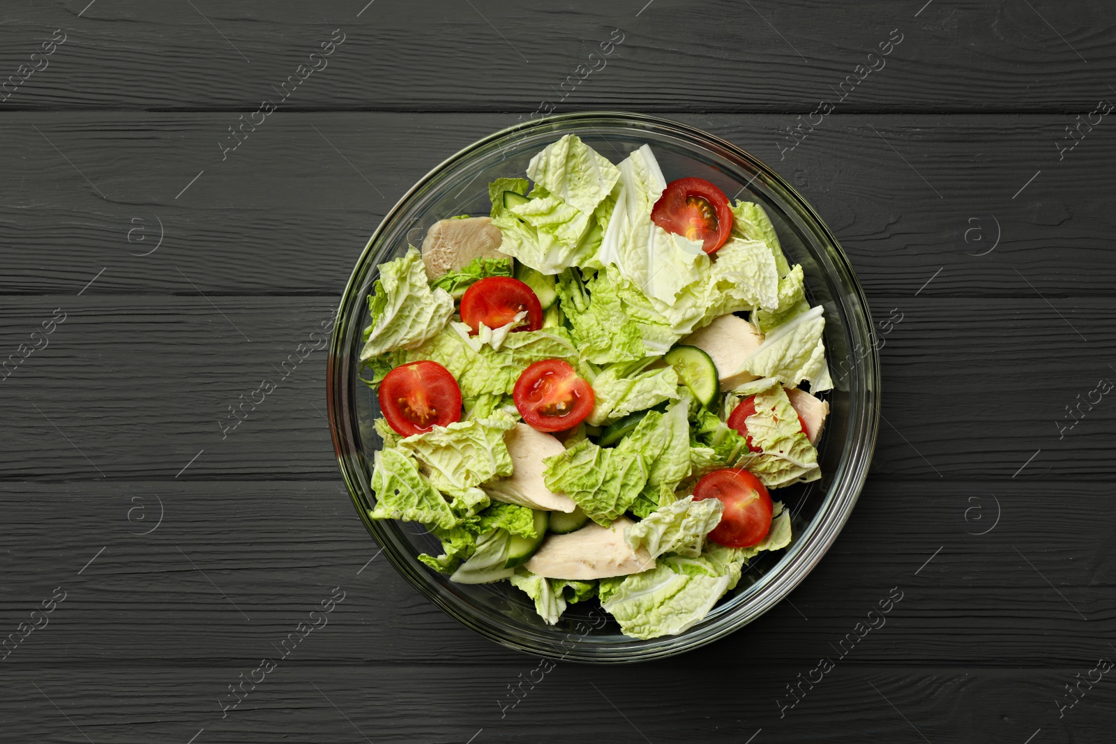 Photo of Bowl of delicious salad with Chinese cabbage, cucumber and tomatoes on black wooden table, top view