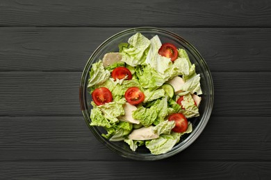 Photo of Bowl of delicious salad with Chinese cabbage, cucumber and tomatoes on black wooden table, top view