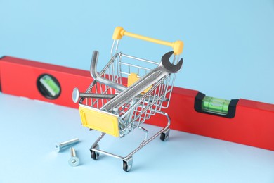 Photo of Shopping cart with different construction tools on light blue background