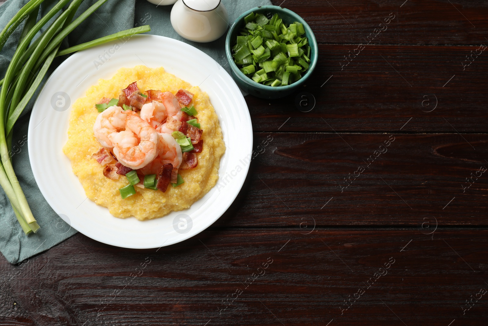 Photo of Plate with fresh tasty shrimps, bacon, grits and green onion on dark wooden table, flat lay. Space for text