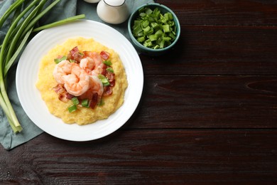 Plate with fresh tasty shrimps, bacon, grits and green onion on dark wooden table, flat lay. Space for text