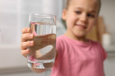 Photo of Cute little girl holding glass of fresh water indoors, selective focus
