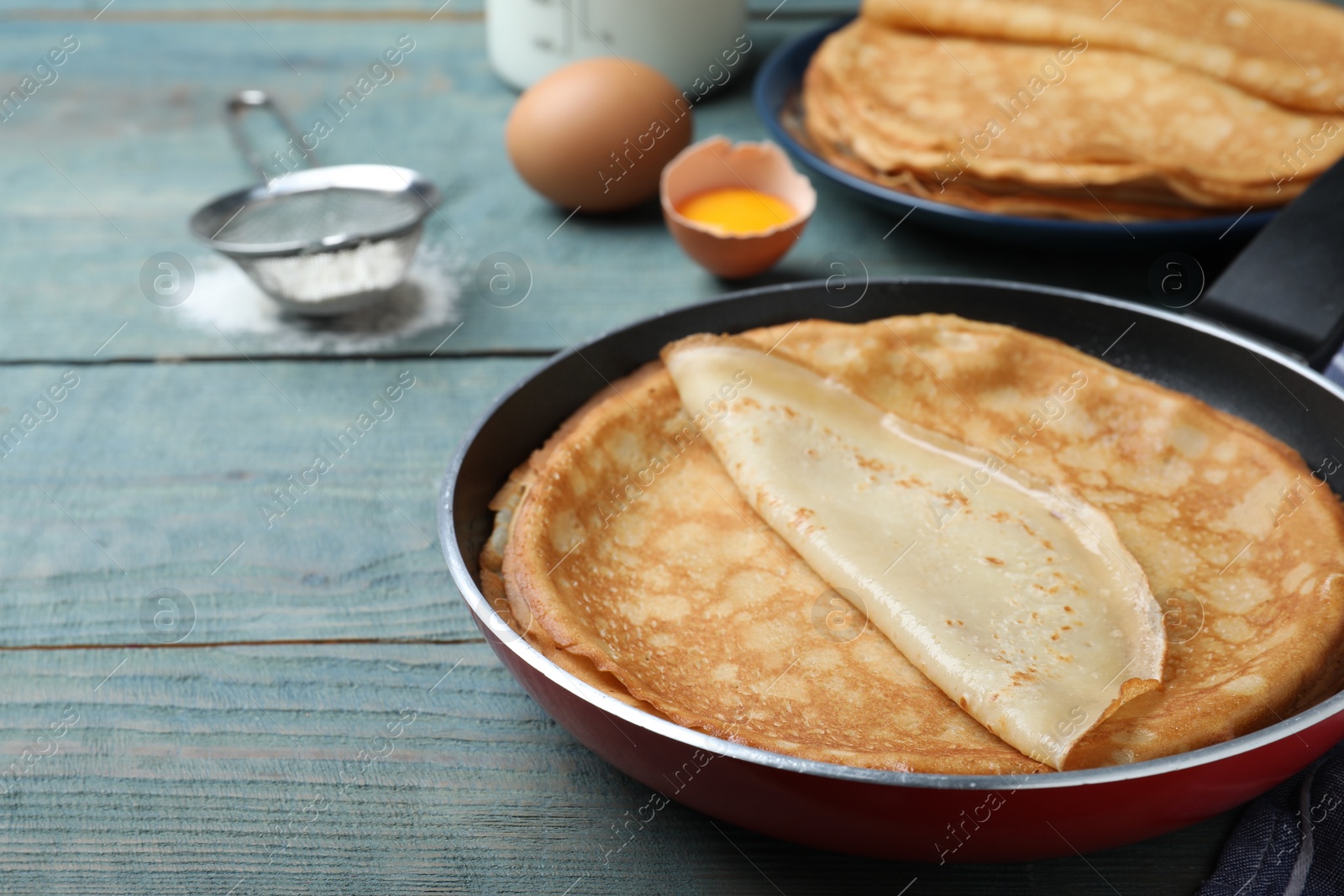 Photo of Delicious thin pancakes on blue wooden table, closeup