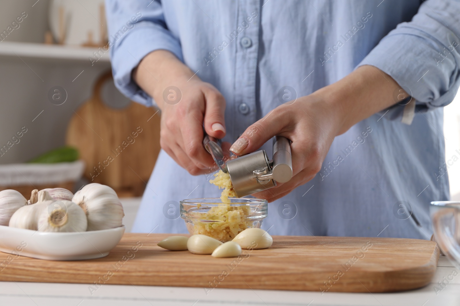 Photo of Woman squeezing garlic with press at white table in kitchen, closeup