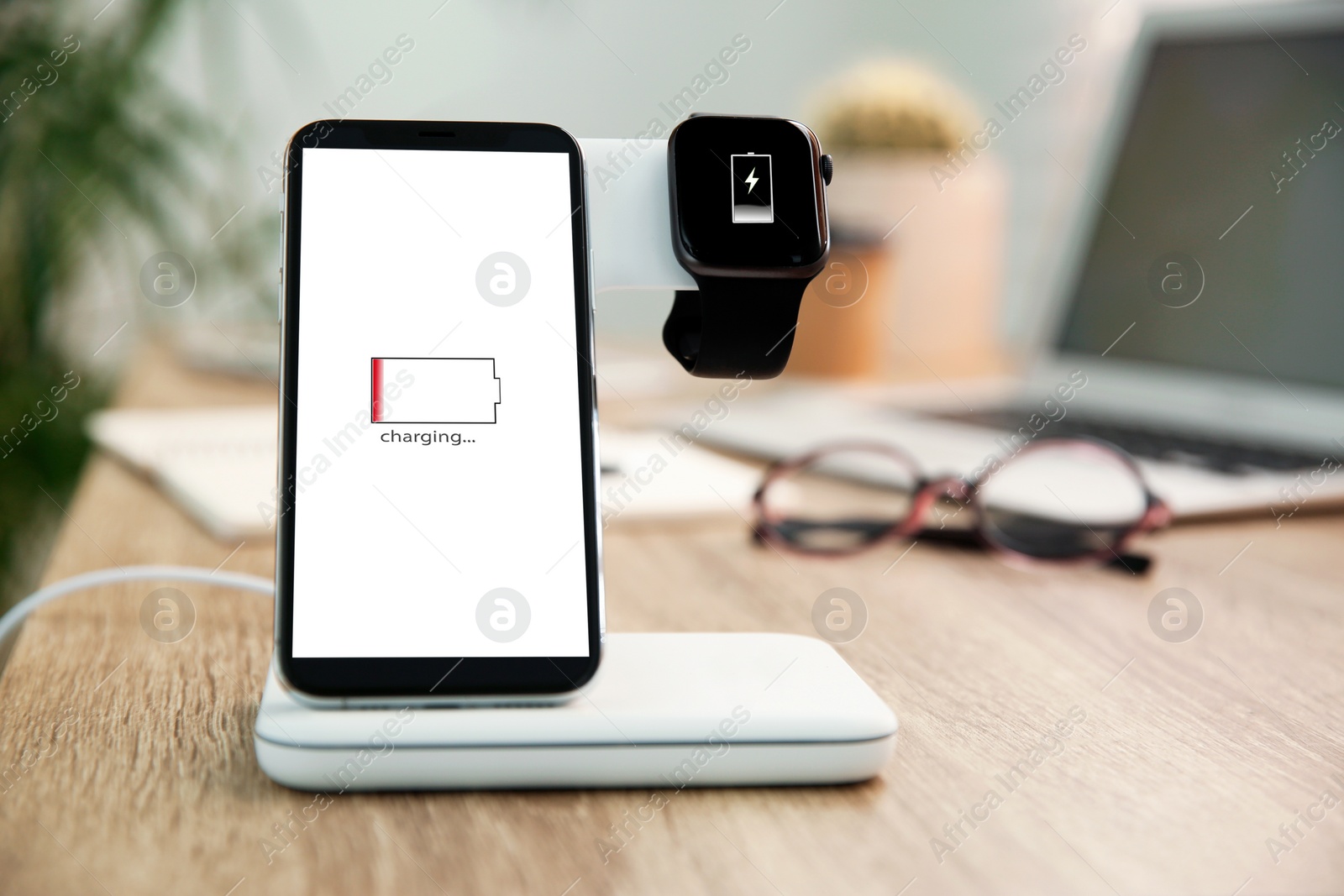 Photo of Mobile phone and smartwatch with wireless charger on wooden table. Modern workplace accessory