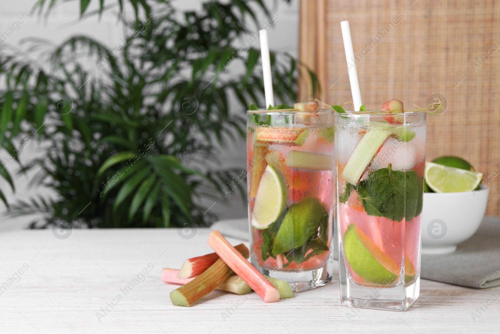 Photo of Tasty rhubarb cocktail with lime on white wooden table indoors, space for text