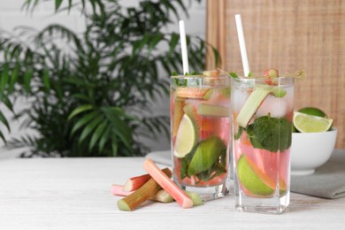 Tasty rhubarb cocktail with lime on white wooden table indoors, space for text