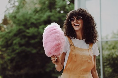 Smiling woman with cotton candy outdoors. Space for text