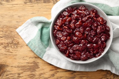 Photo of Tasty dried cranberries in bowl on wooden table, top view. Space for text